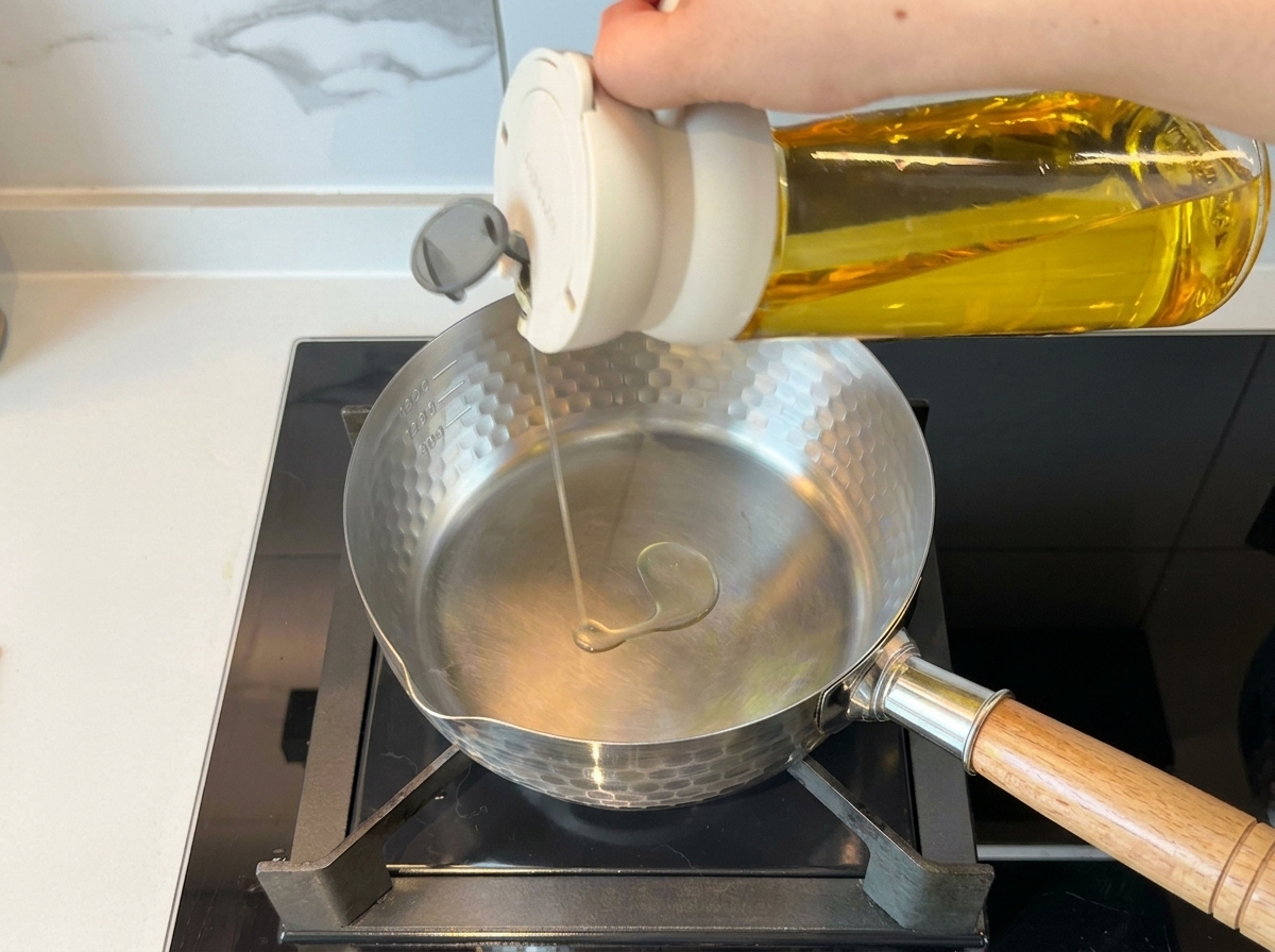 Une main versant de lhuile de cuisson dans une casserole en acier inoxydable sur une cuisinière.