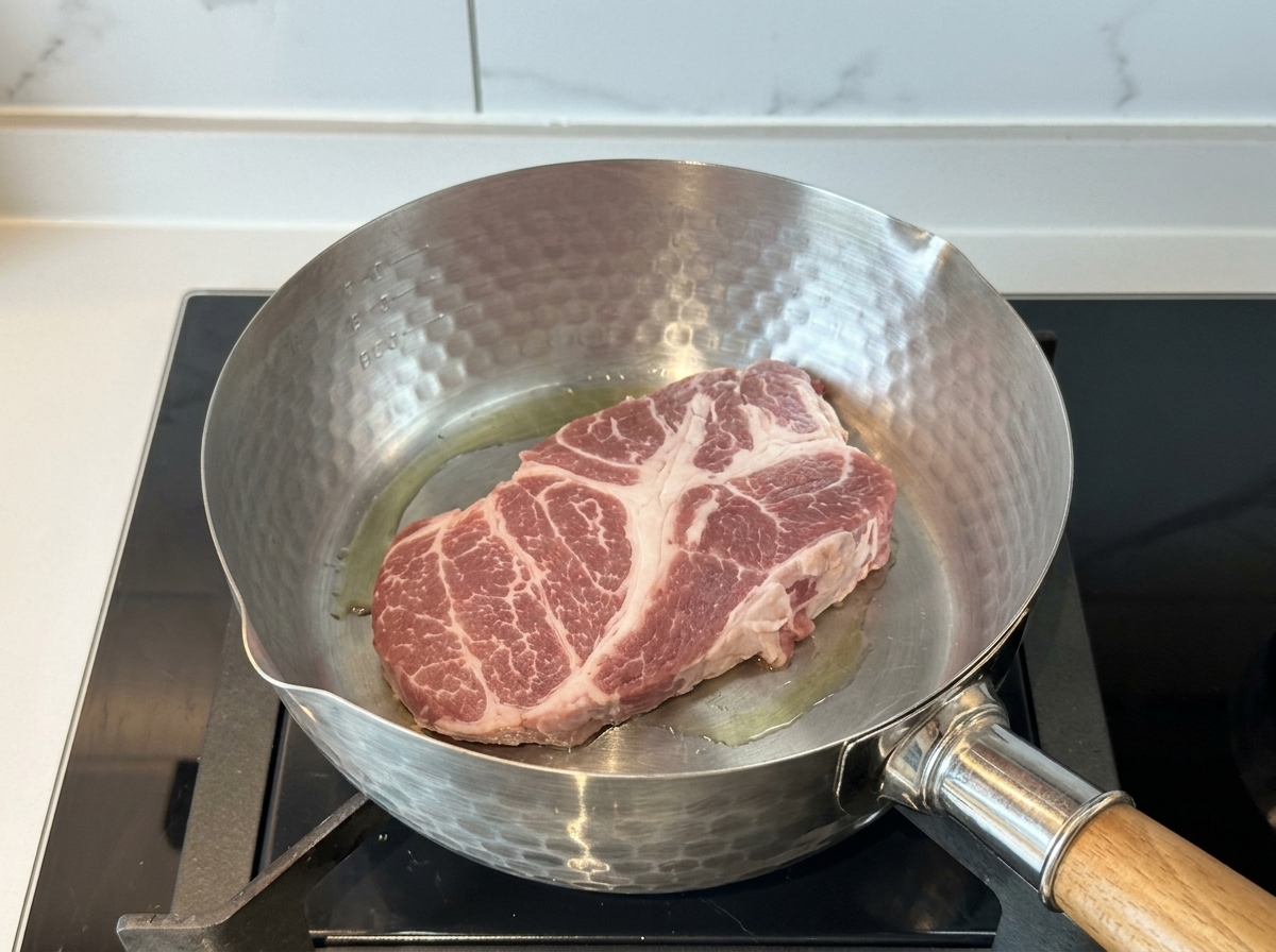 Une tranche épaisse déchine de porc crue saisissant dans une casserole chaude avec un peu dhuile.