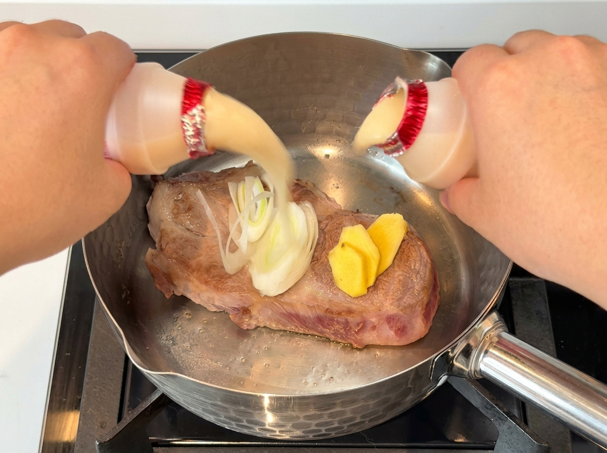 Mains versant deux petites bouteilles de boisson lactée sur un morceau de porc saisi avec des oignons et du gingembre.