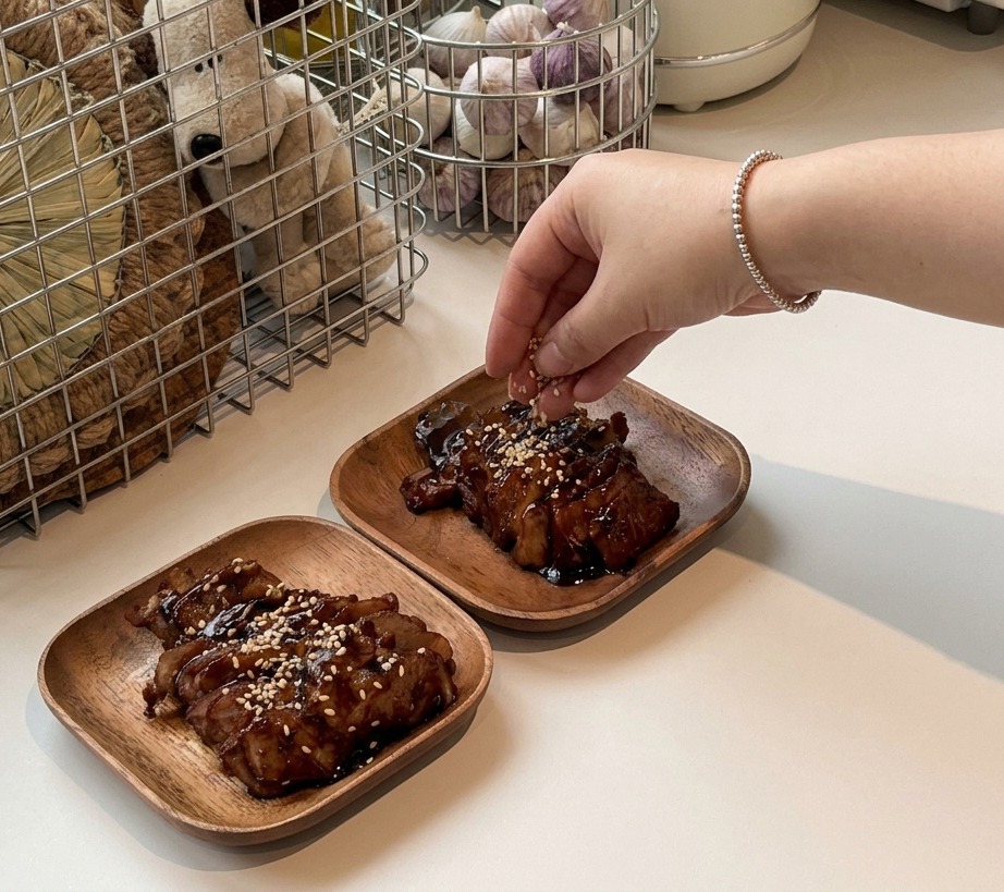 Une main saupoudrant des graines de sésame blanc sur les tranches de porc laqué présentées sur des petites assiettes.