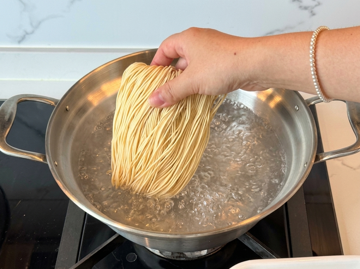 Une main ajoutant un paquet de nouilles ramen sèches dans une casserole deau bouillante.