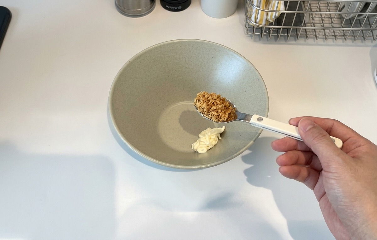 Une main tenant une cuillère dail frit au-dessus dun bol contenant une noisette de mayonnaise.