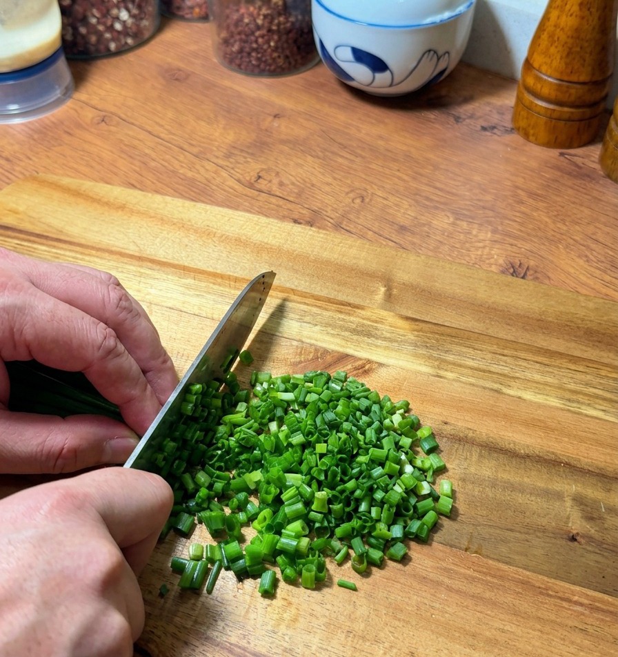 Mains coupant soigneusement des oignons verts frais sur une planche en bois.