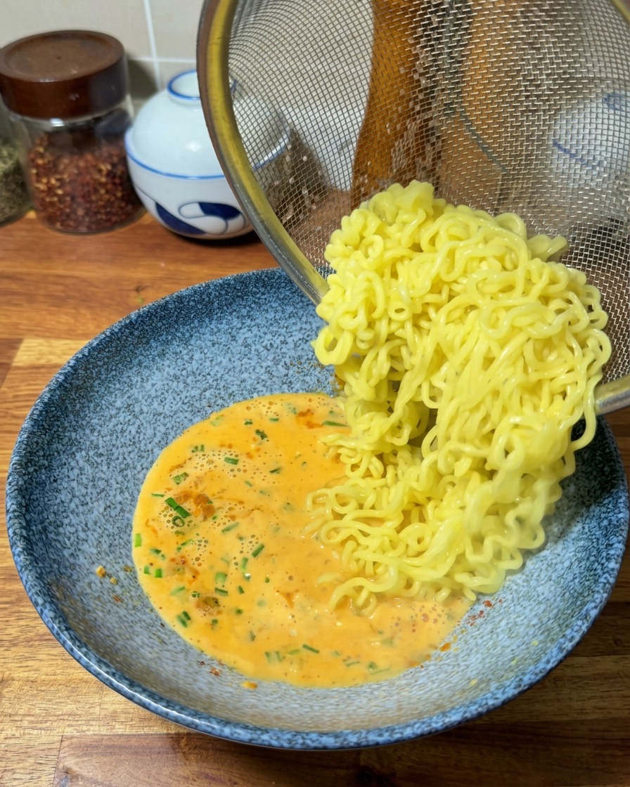Nouilles ramen égouttées glissant dans le bol de bouillon crémeux.
