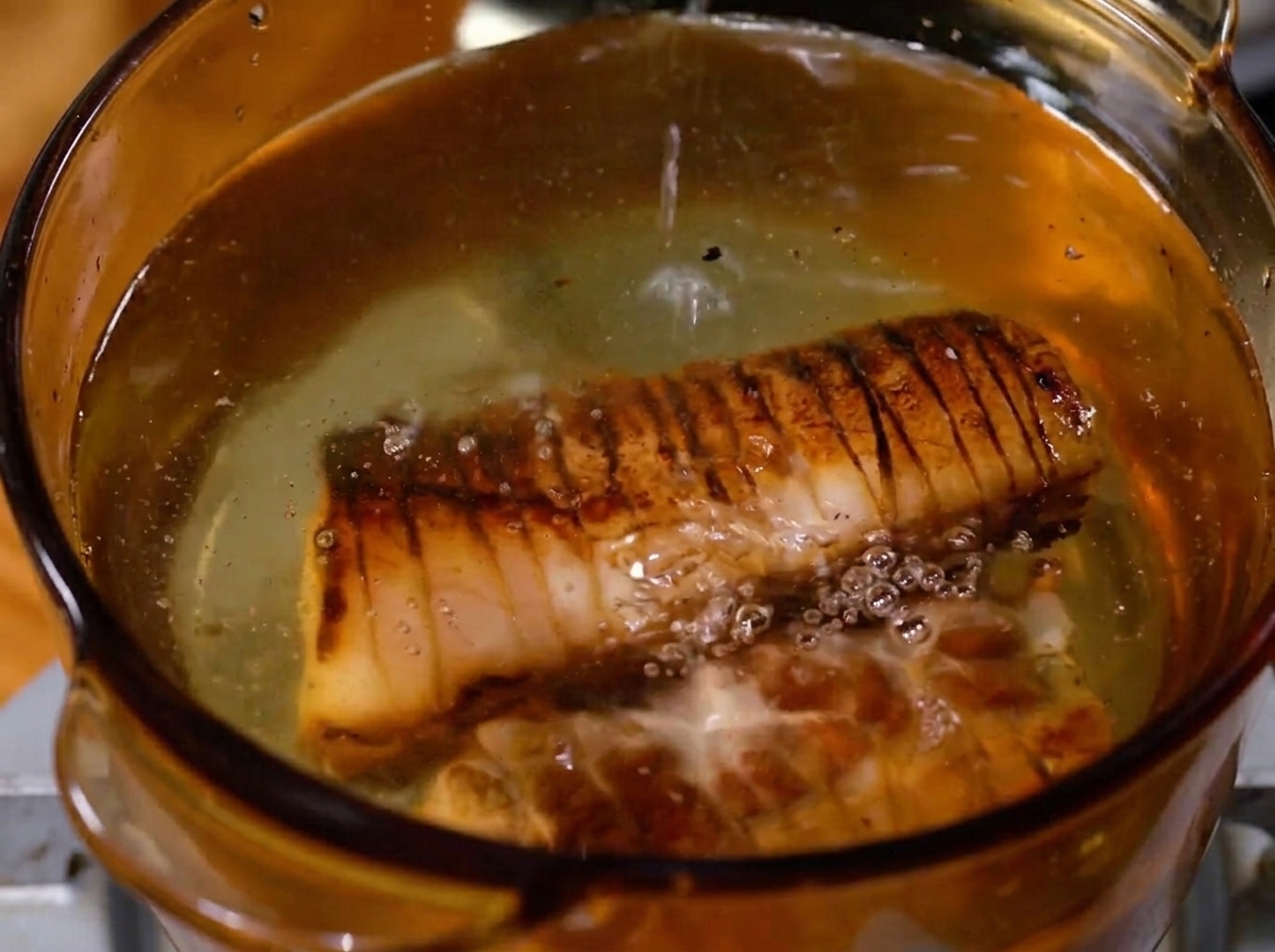 Un morceau de poitrine de porc saisie frémissant dans une marmite de liquide bouillonnant.
