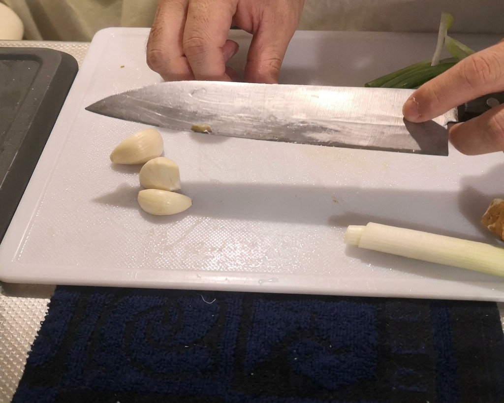 Une personne appuyant avec la lame plate dun grand couteau de cuisine sur des gousses dail pelées pour les écraser sur une planche à découper.