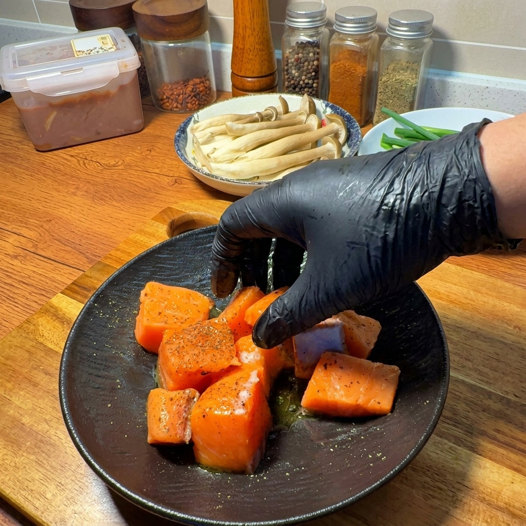 Une main gantée mélangeant les morceaux de saumon crus avec lassaisonnement et lhuile sur une assiette.