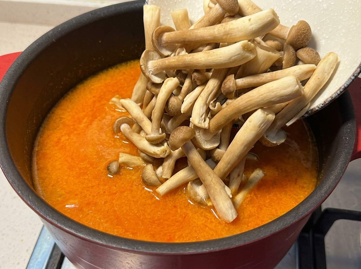 Champignons shimeji versés depuis un bol dans une casserole de bouillon frémissant orangé.