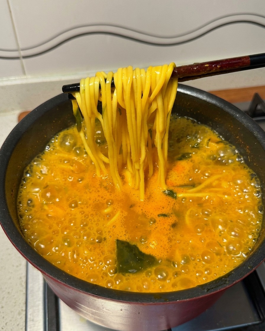 Baguettes noires soulevant des nouilles ramen jaunes dune soupe épicée bouillonnante.