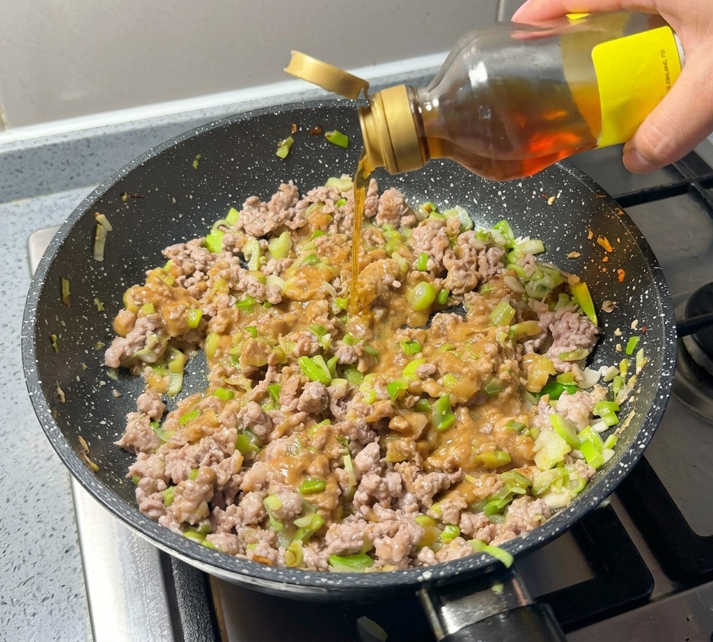 Huile de sésame versée directement sur le mélange de viande et miso dans la poêle.