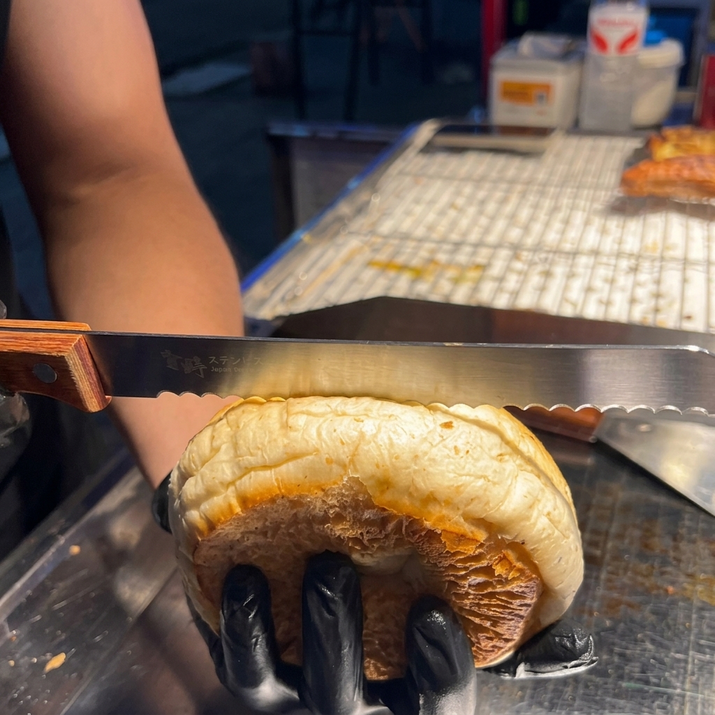 Une main utilisant un couteau dentelé pour couper délicatement un pain à burger en deux horizontalement.