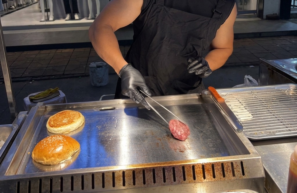 Une personne déposant une boule de bœuf haché cru sur une plaque métallique brûlante à laide de pinces.