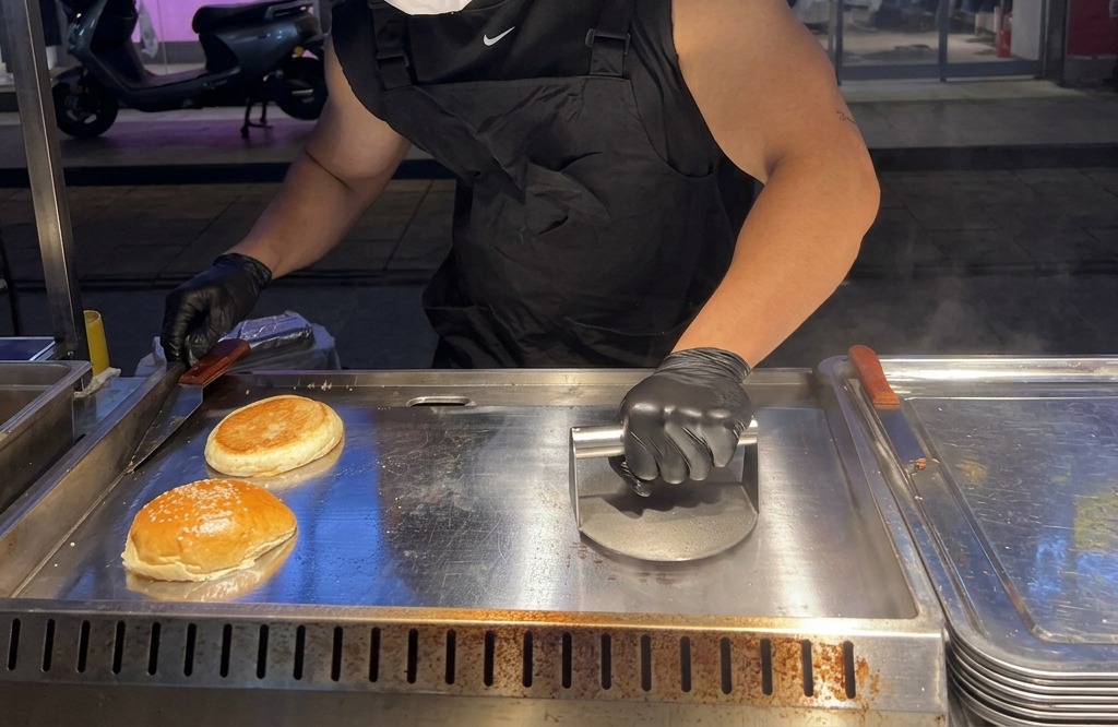 Une personne utilisant une presse à burger lourde pour aplatir fermement une boule de bœuf sur une plaque chaude.
