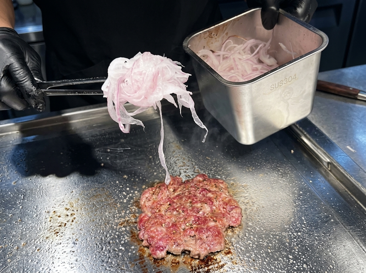 Une poignée doignons rouges très finement émincés déposée sur un steak de bœuf en cours de cuisson.