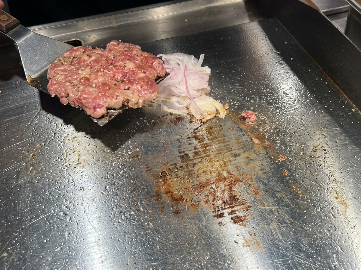 Une spatule métallique retournant un steak de bœuf bien doré sur un lit doignons sur la plaque.