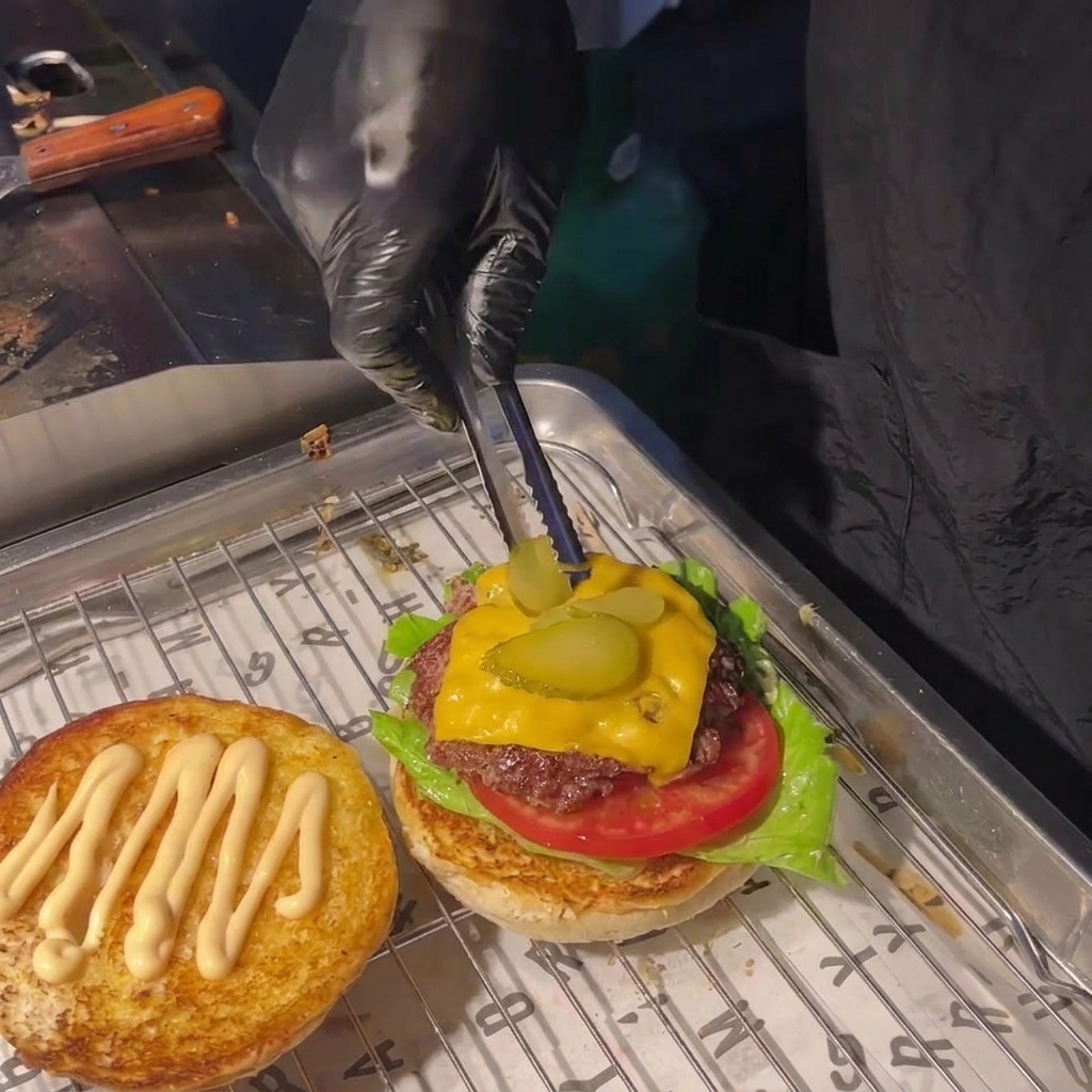 Une personne utilisant des pinces pour disposer deux tranches de cornichons sur le fromage fondu du steak.