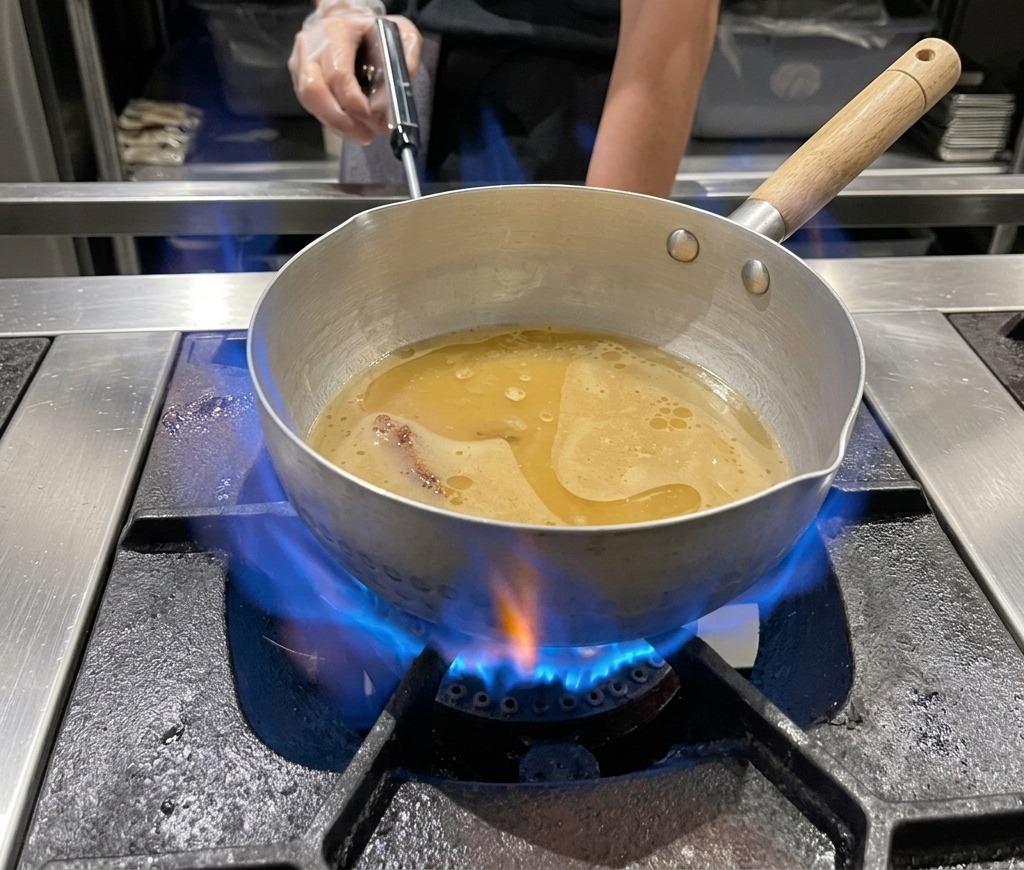 Une casserole de bouillon de ramen au miso mijotant sur une flamme de gaz bleue.