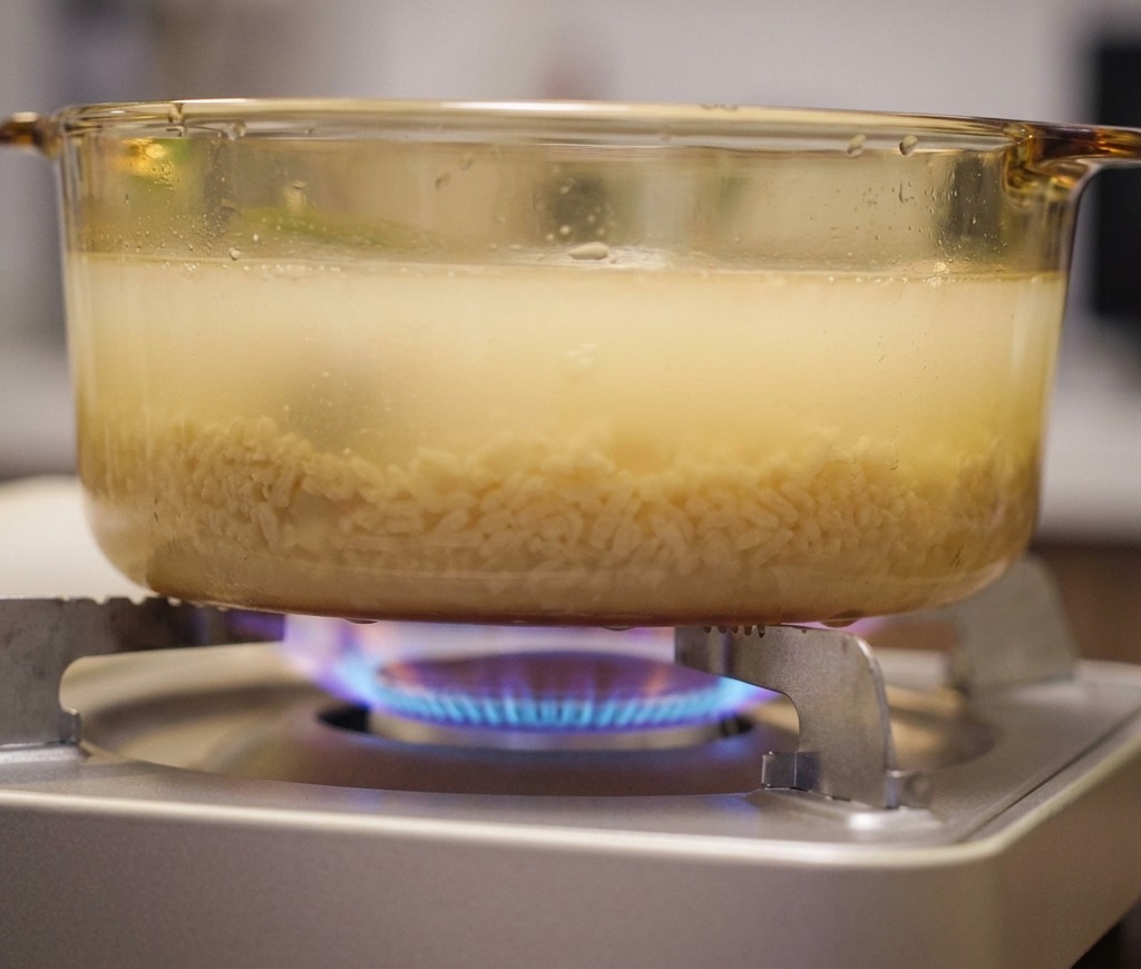 Une marmite en verre avec un bouillon de ramen laiteux mijotant sur un réchaud à gaz.