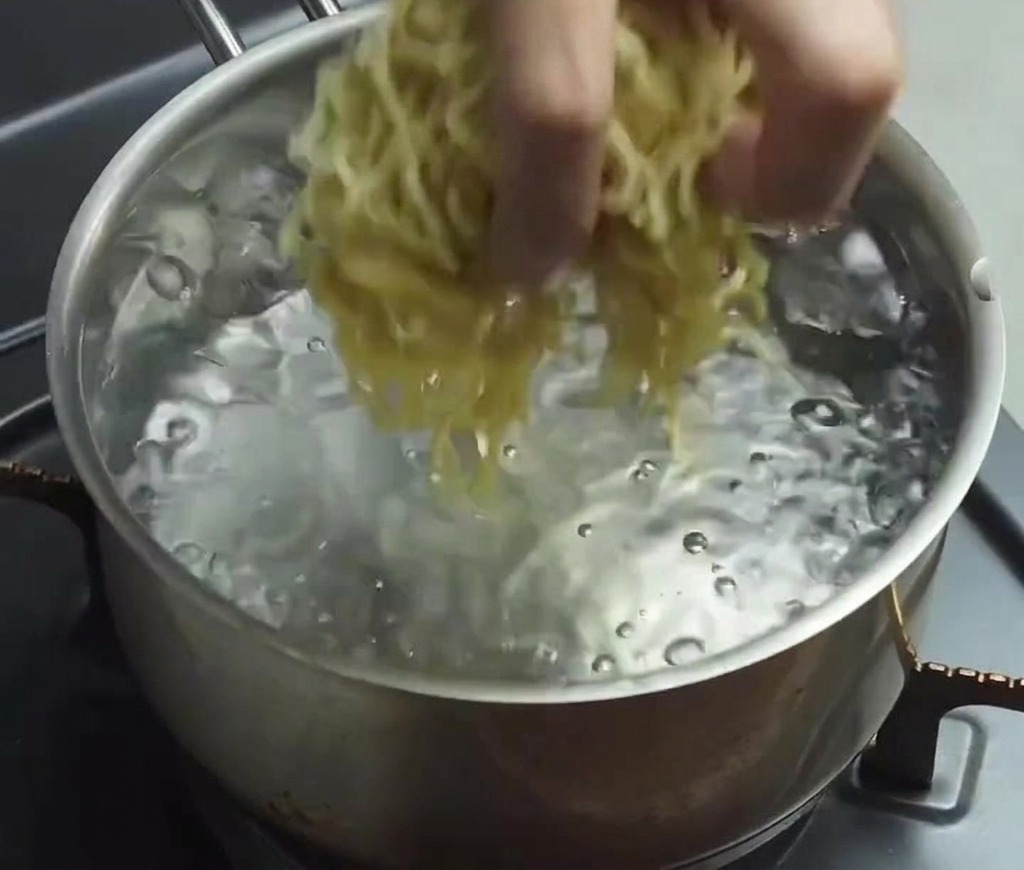 Main déposant un nid de nouilles ramen fraîches dans de leau bouillante à gros bouillons.