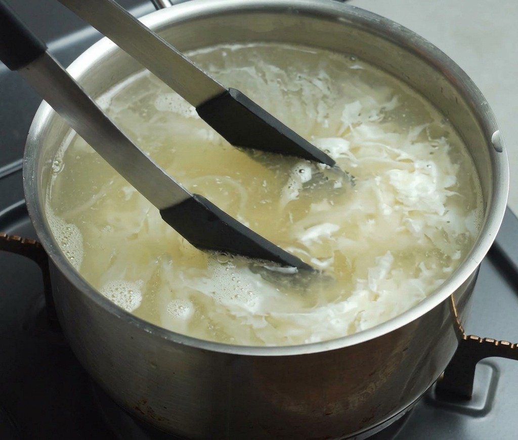 Pinces de cuisine remuant les nouilles jaunes dans leau bouillante sur la cuisinière.