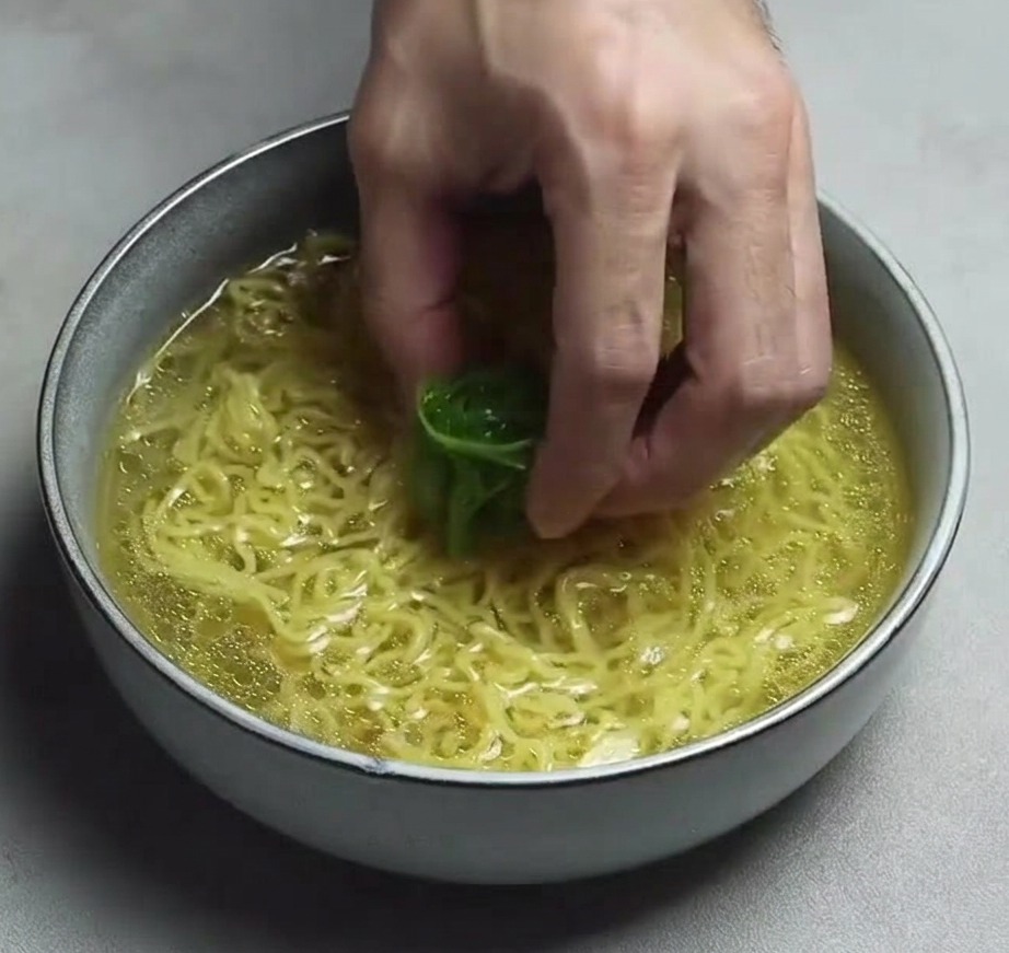 Main déposant des oignons verts émincés sur les nouilles dans le bol.