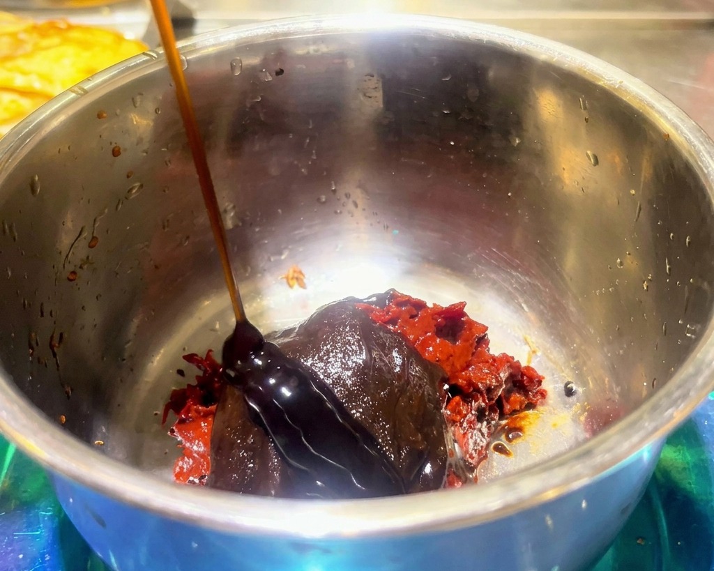 Une sauce sombre et épaisse versée sur de la pâte de soja rouge et de lassaisonnement pour fondue dans un bol en inox.