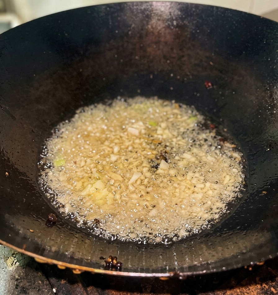 Oignons verts hachés crépitant dans lhuile chaude au fond dun wok en fonte sombre.