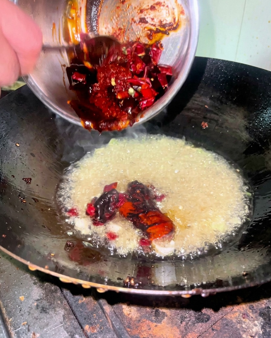 Un mélange de sauce rouge épais versé dun bol en inox dans un wok contenant lhuile et les aromates.