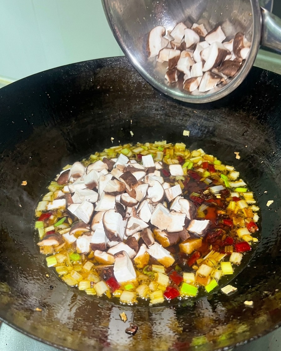 Dés de poulet blanc et shiitakés bruns ajoutés à une sauce rouge riche dans un wok noir.