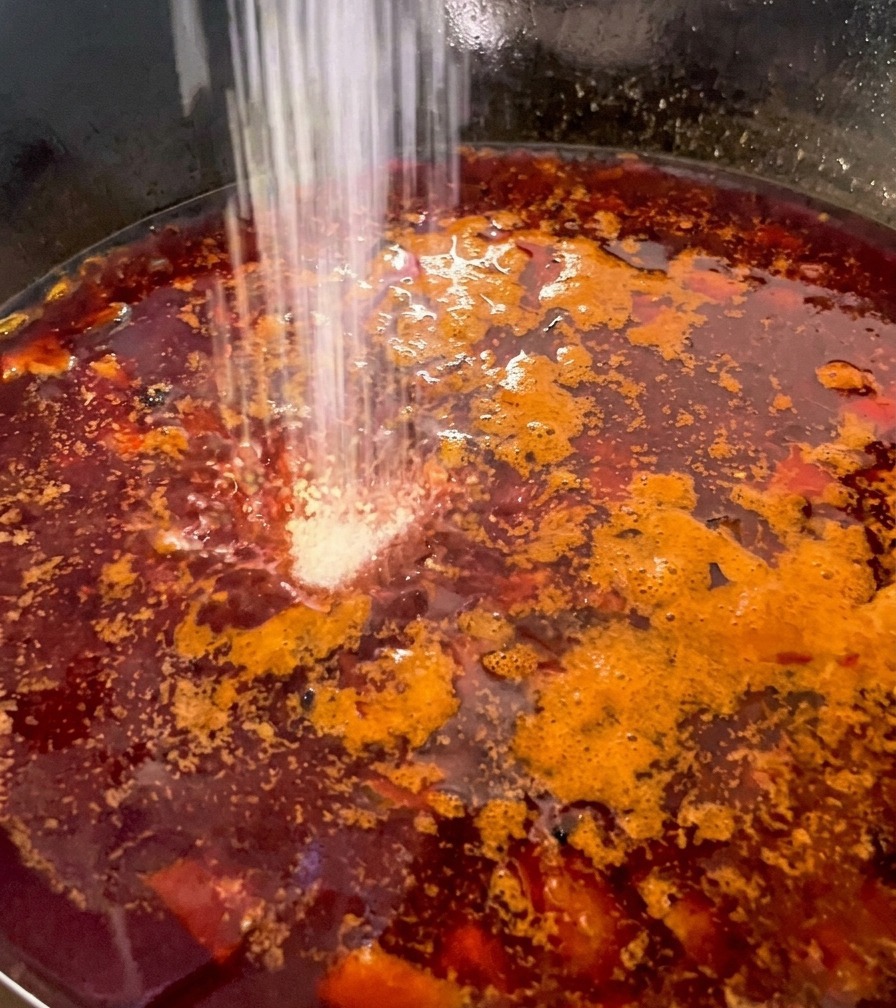 Assaisonnement en poudre blanche saupoudré dans un bouillon rouge bouillonnant contenant poulet et champignons.