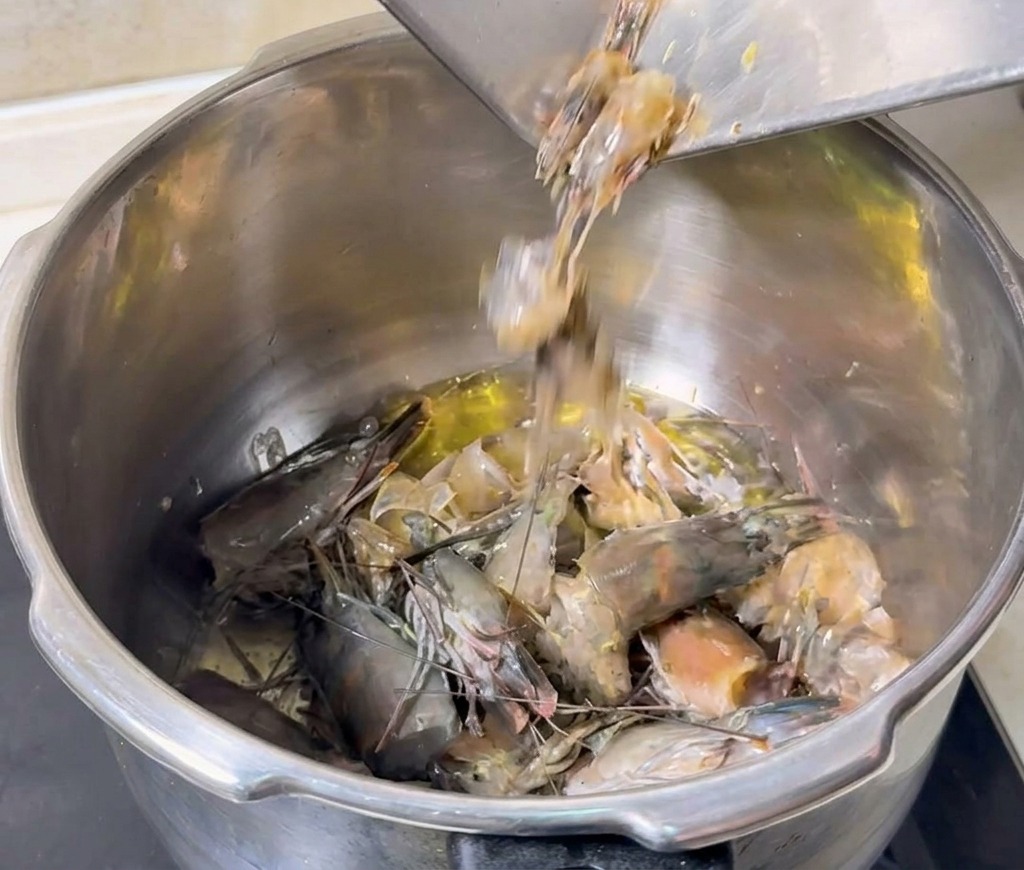 Têtes et carapaces de crevettes grises versées dans une marmite dhuile chaude pour être frites.