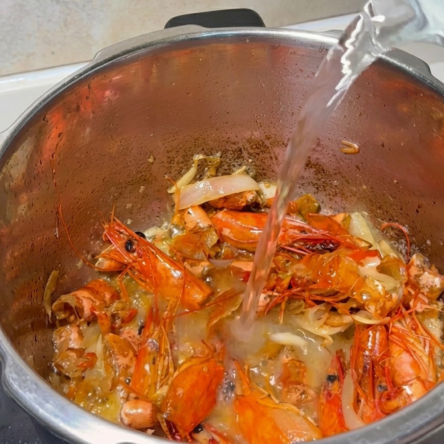 Filet deau versé dans une marmite remplie de carapaces de crevettes et daromates sautés.