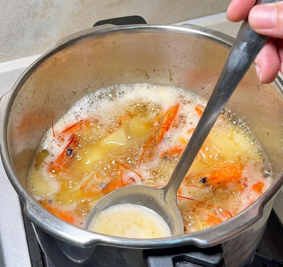 Une louche remuant un bouillon de crevettes bouillonnant avec du beurre en train de fondre.