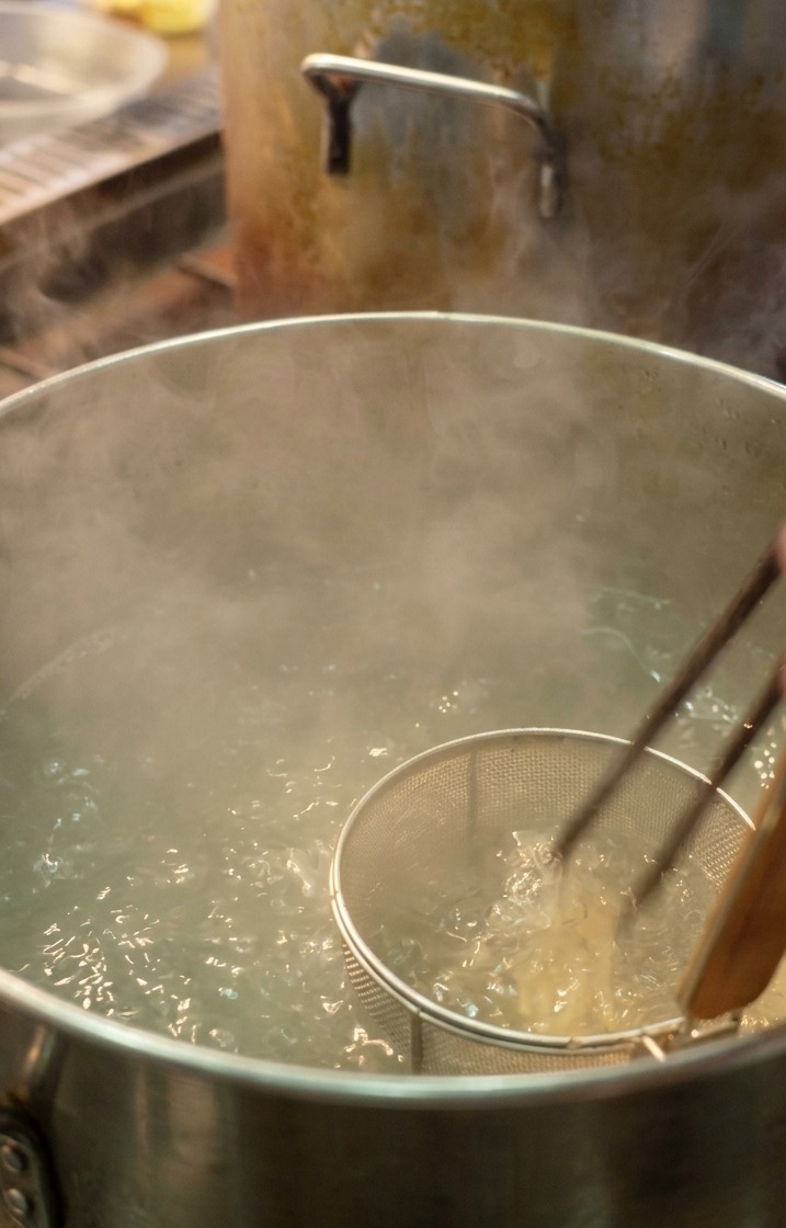 Un chef utilisant une passoire à ramen pour plonger des nouilles blanches dans une grande casserole deau bouillante.