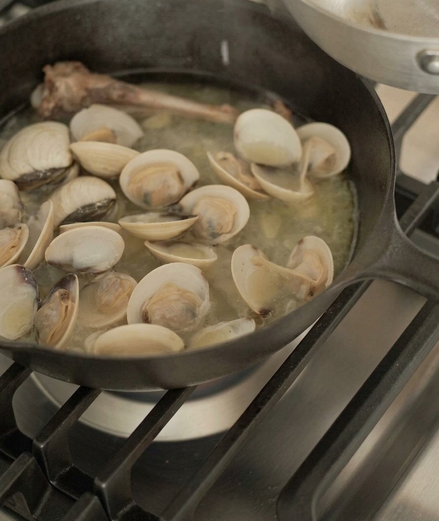Palourdes retirées dune poêle contenant un os de canard et un bouillon savoureux à laide de pinces en métal.