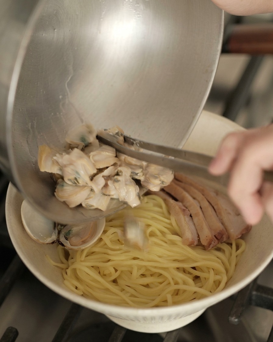 Palourdes cuites versées dun bol en métal sur un bol de ramen prêt avec les nouilles et le canard.