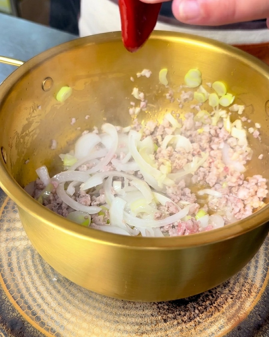 Sauce bibimbap coréenne rouge versée dans une marmite avec le porc sauté et les oignons.