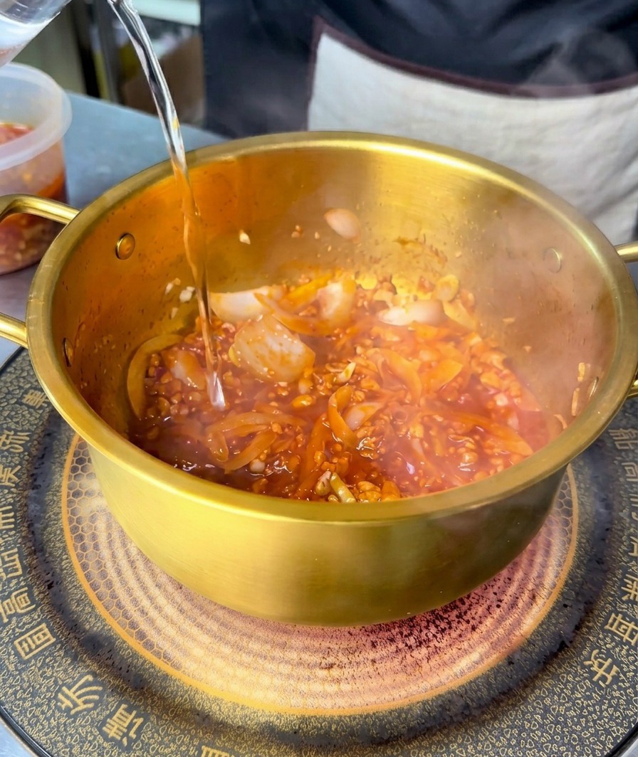 De leau claire versée dans une marmite sur une base de viande et de légumes rouge et épicée.