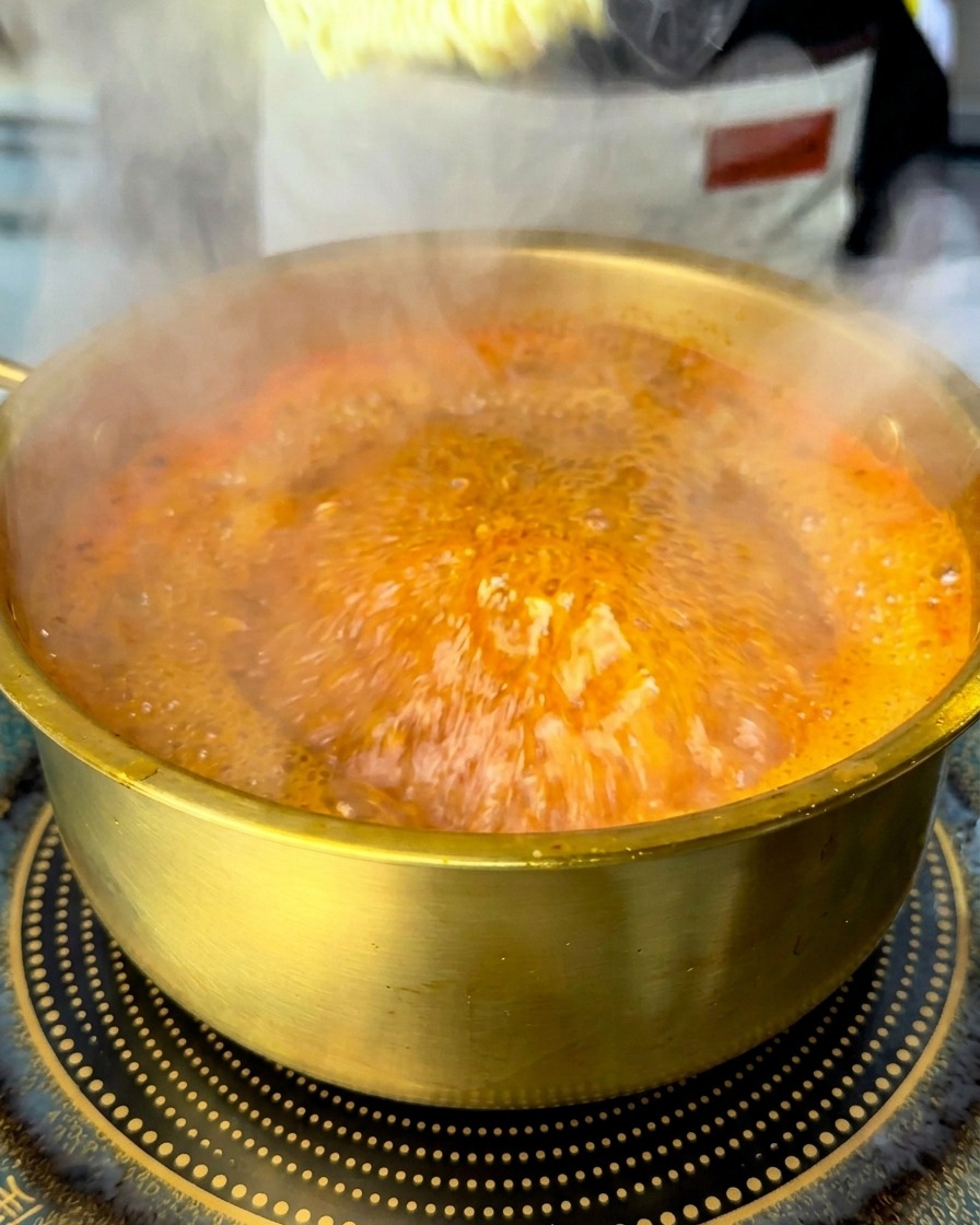Un bloc de nouilles instantanées plongé dans un bouillon rouge bouillonnant.