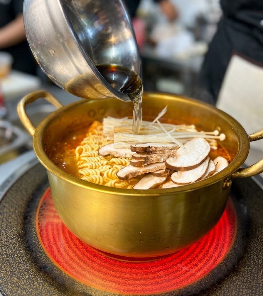 Ajout dun bol de champignons et de fruits de mer dans le bouillon rouge épicé avec les nouilles.