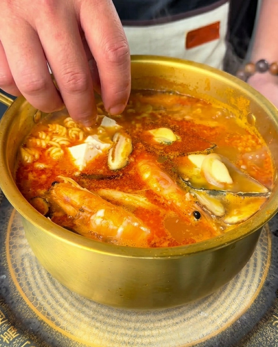 Dépôt de dés de tofu soyeux et de piments frais dans le ramen épicé bouillonnant.