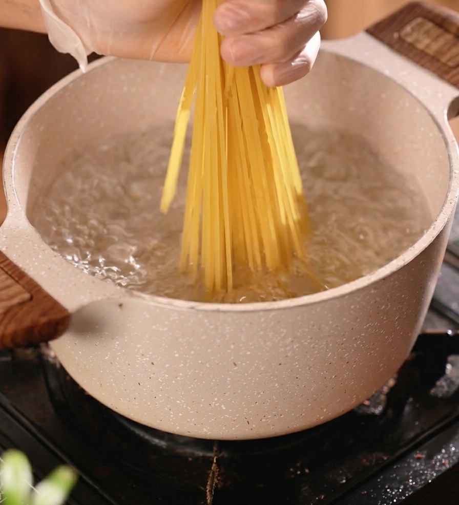 Un faisceau de spaghettis secs plongé dans une casserole deau bouillante.