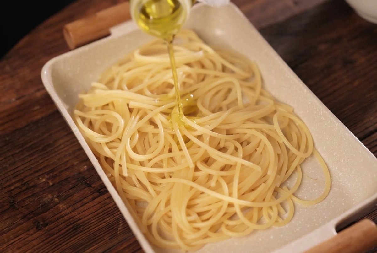 Spaghettis cuits dans un plat rectangulaire, arrosés dhuile dolive dorée.