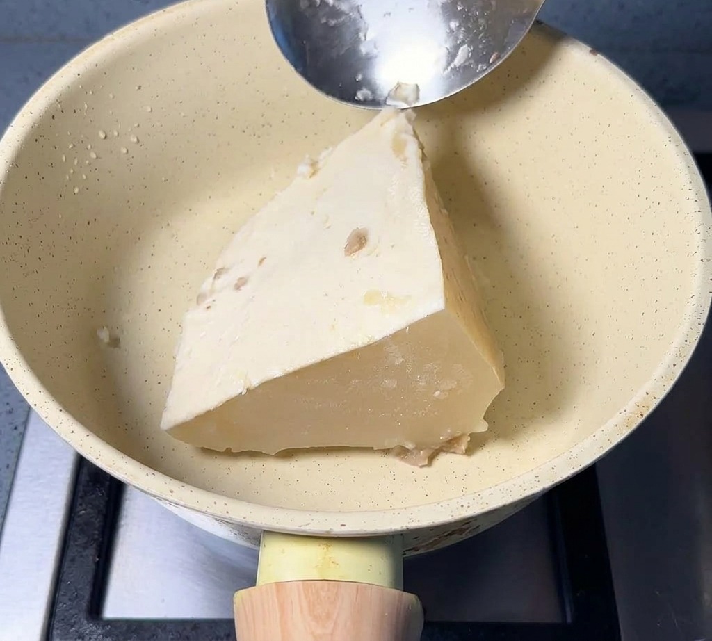 Un bloc triangulaire de bouillon de porc congelé dans une poêle avec une cuillère en métal.