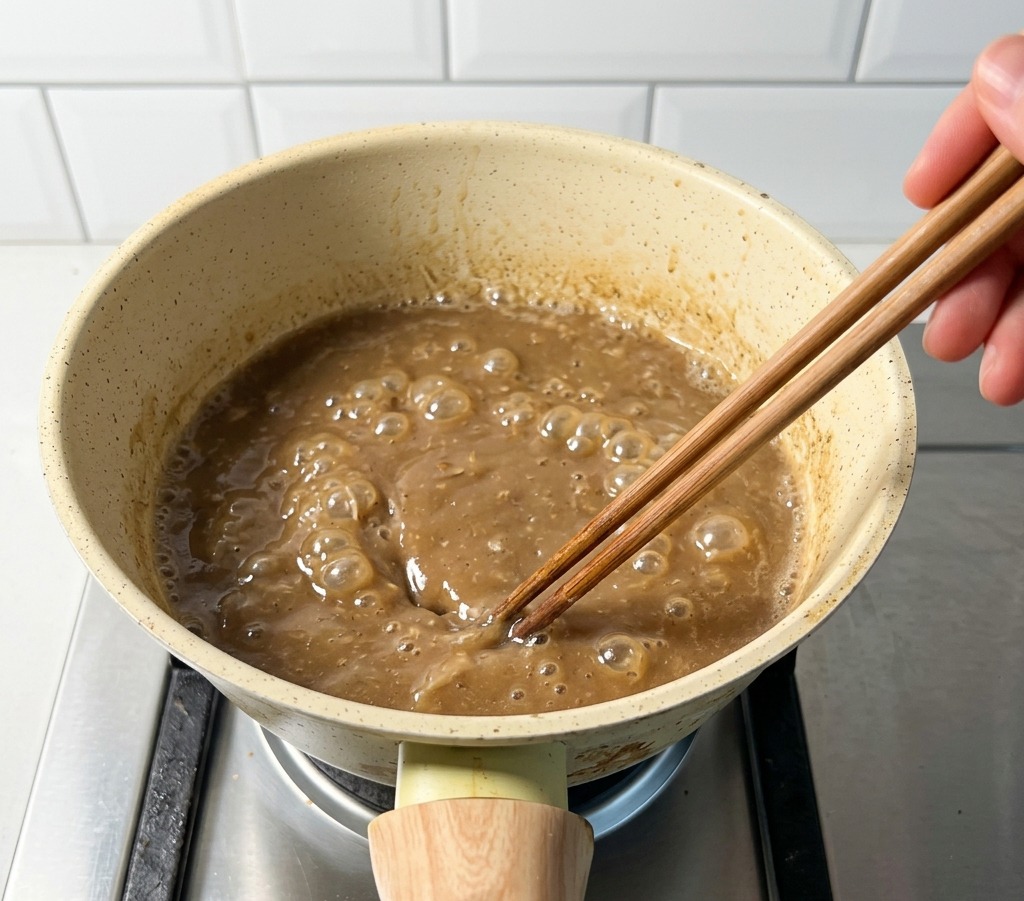 Petite casserole sur une cuisinière à gaz contenant un bouillon de porc et poisson bouillonnant remué avec des baguettes.