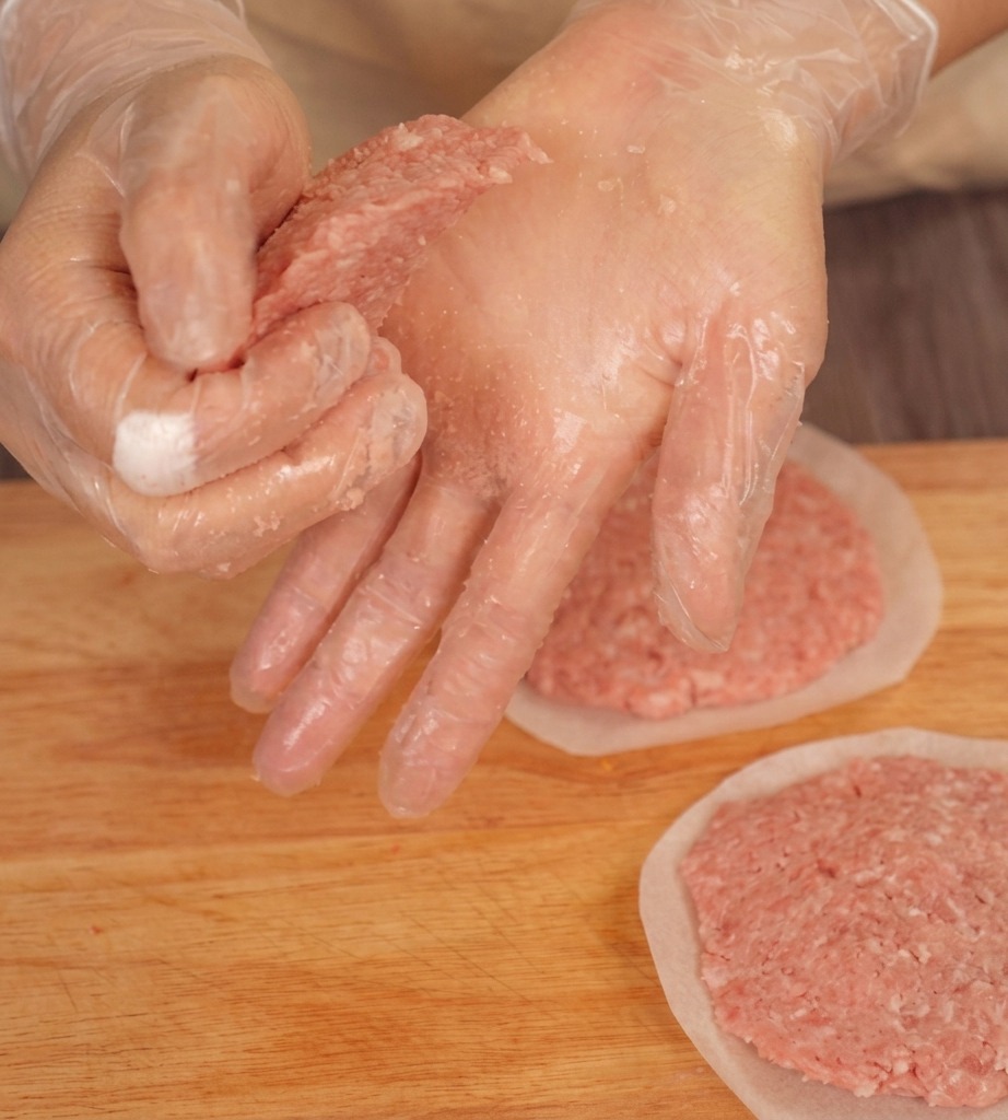Mains gantées pressant les bords dun steak de bœuf cru sur une planche pour créer une forme biseautée.
