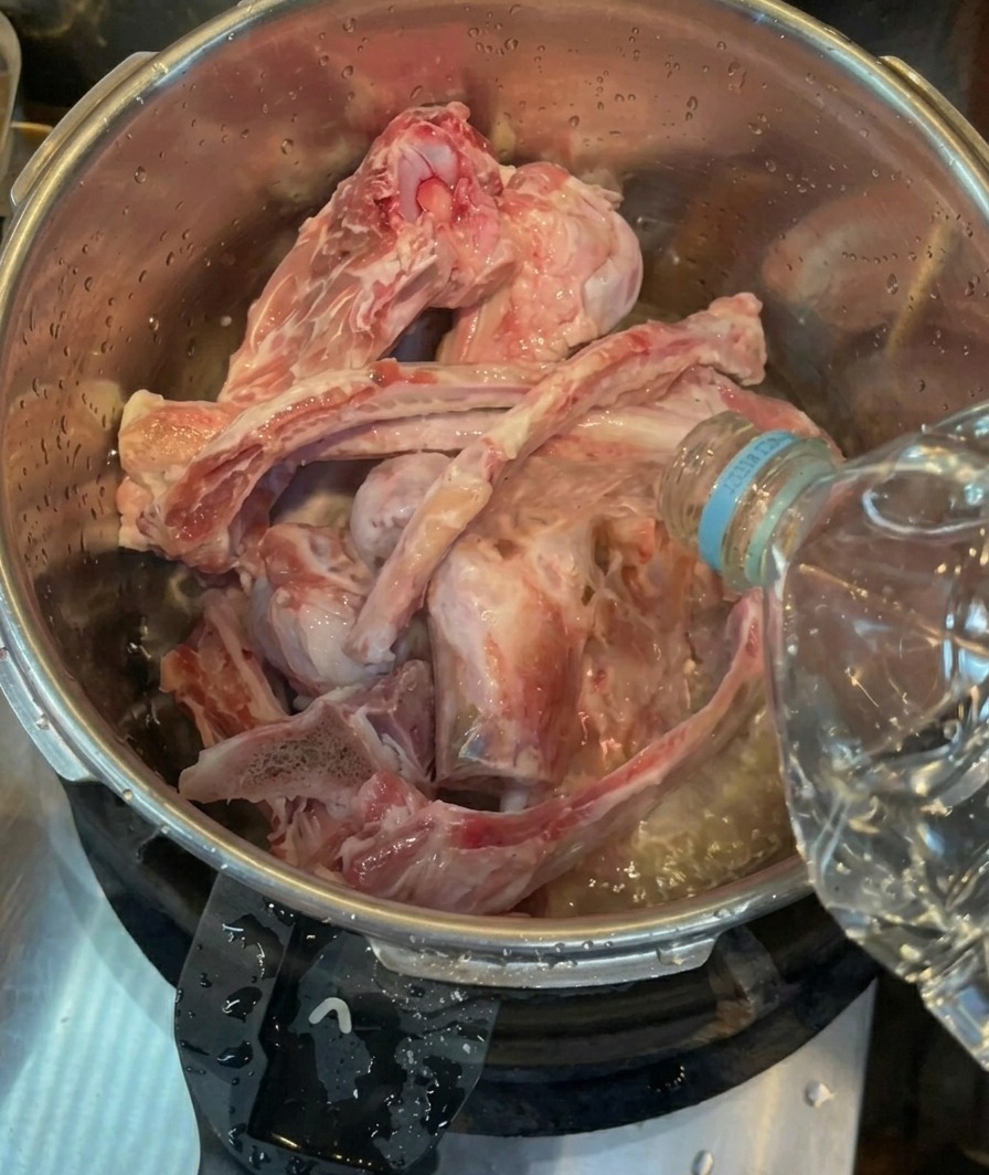 De leau en bouteille versée sur des os de porc crus et nettoyés dans la cuve en acier inoxydable dun autocuiseur.