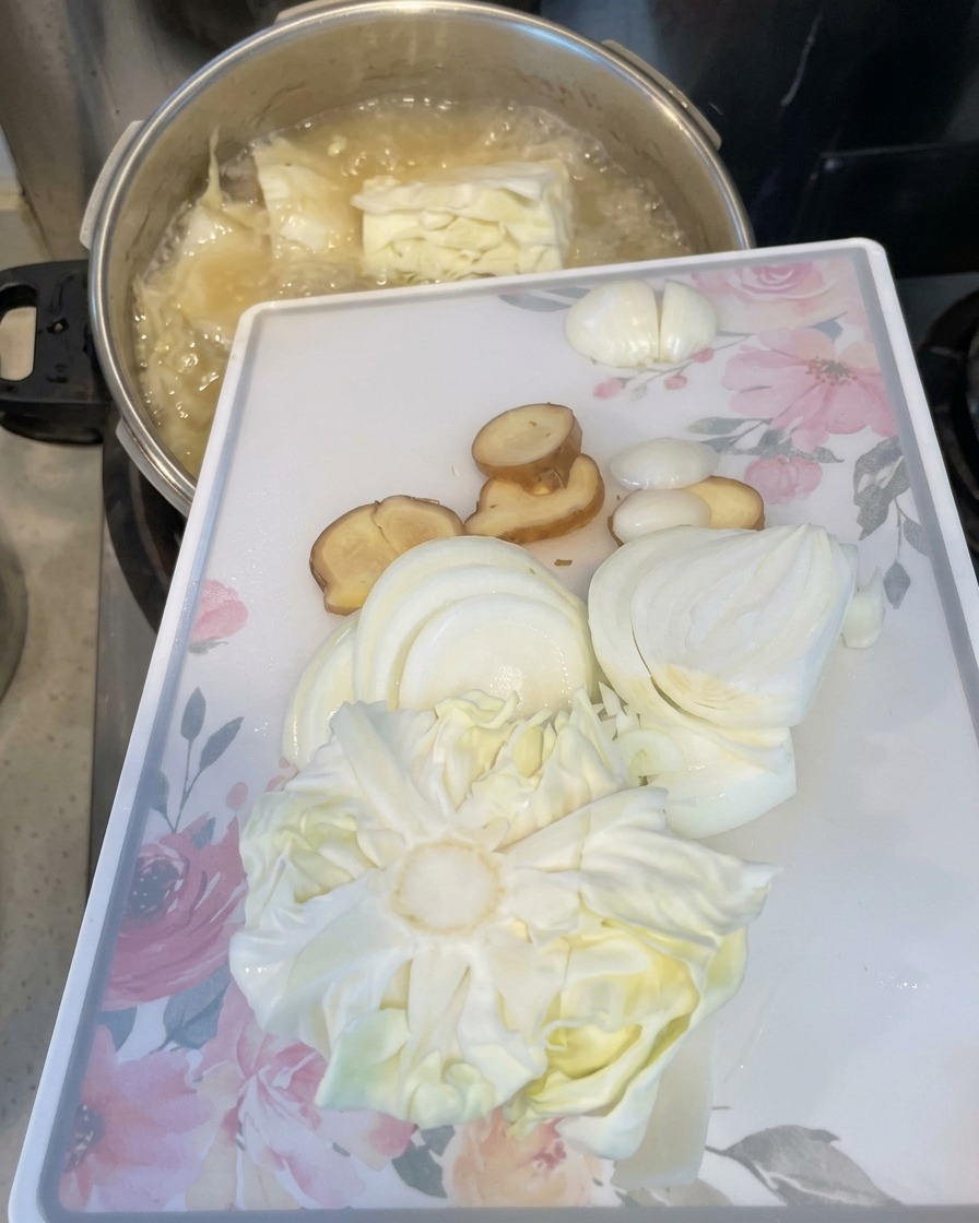Une planche à découper blanche inclinée pour faire glisser des tranches doignons, de gingembre et de chou dans une marmite en ébullition.