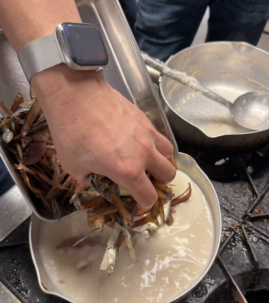 La main dun chef ajoute une poignée dingrédients séchés de couleur brun foncé dans une casserole de bouillon blanc crémeux.