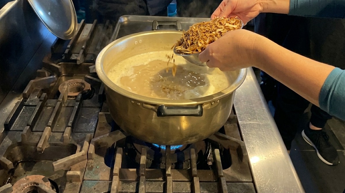 Mains ajoutant une poignée danchois séchés dans une grande marmite en laiton remplie dun bouillon blanc crémeux.